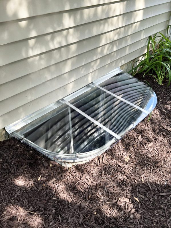 52x25 sloped polycarbonate window well cover surrounded by mulch