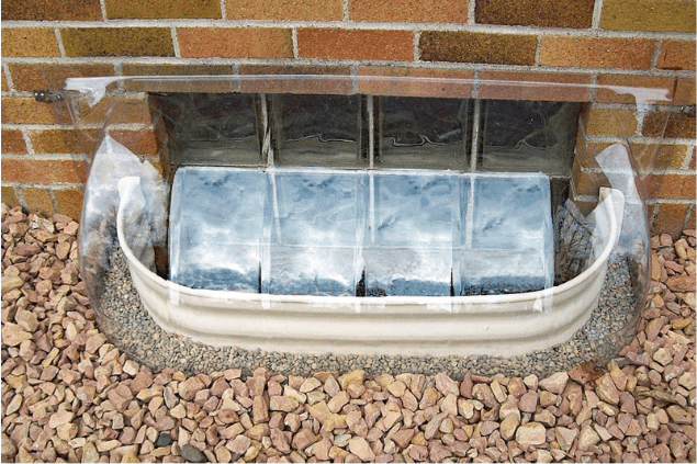 bubble window well cover on brick wall surrounded by decorative rocks