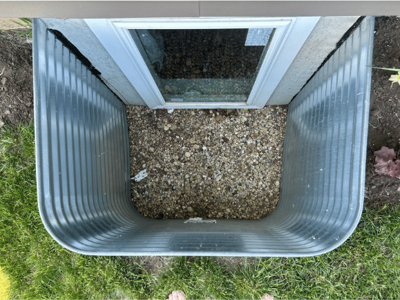 galvanized steel metal window well with pebbles at the bottom of the well